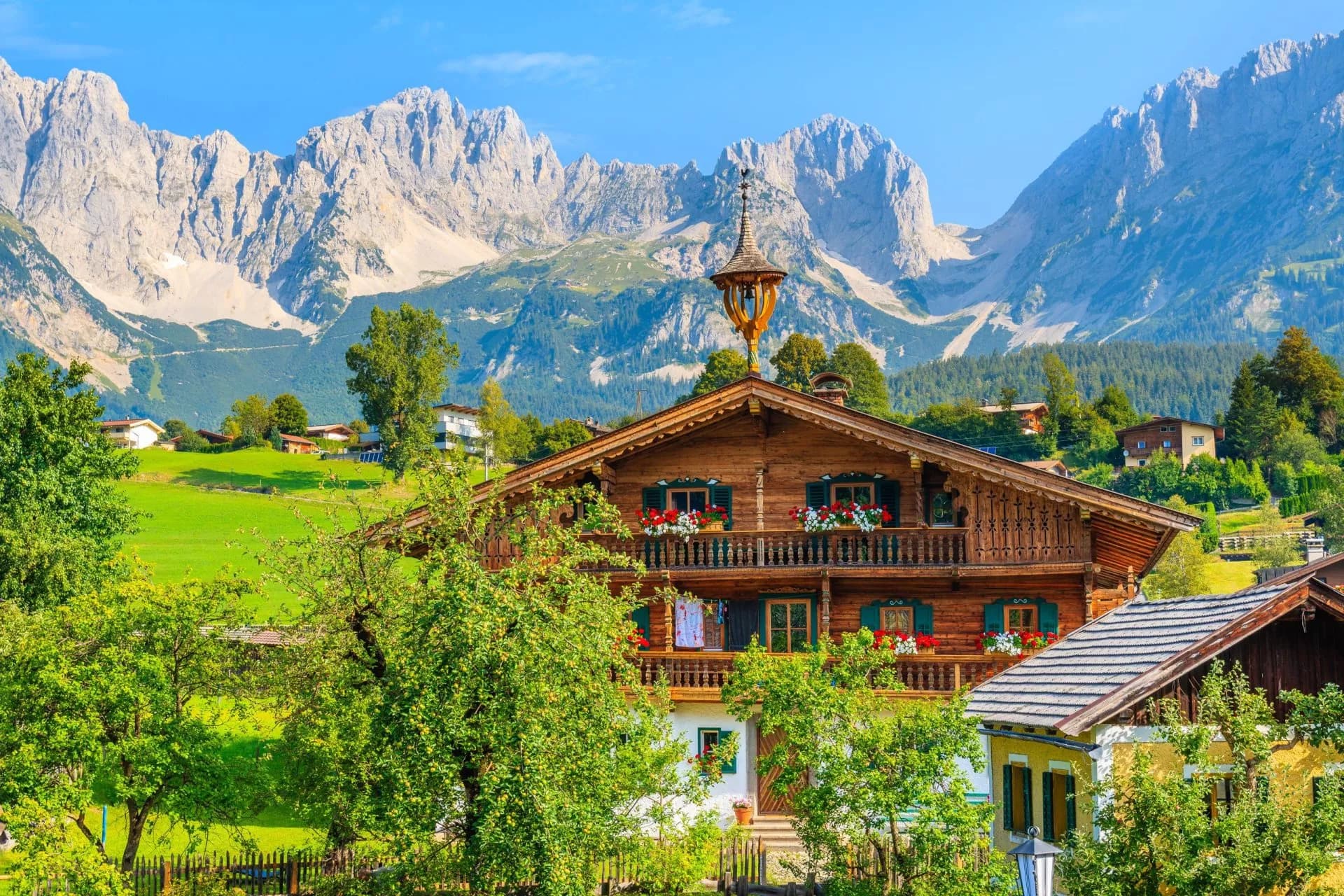 Typical wooden alpine house against Alps mountains background on green meadow in Going am Wilden Kaiser village on sunny summer day, Tyrol, Austria