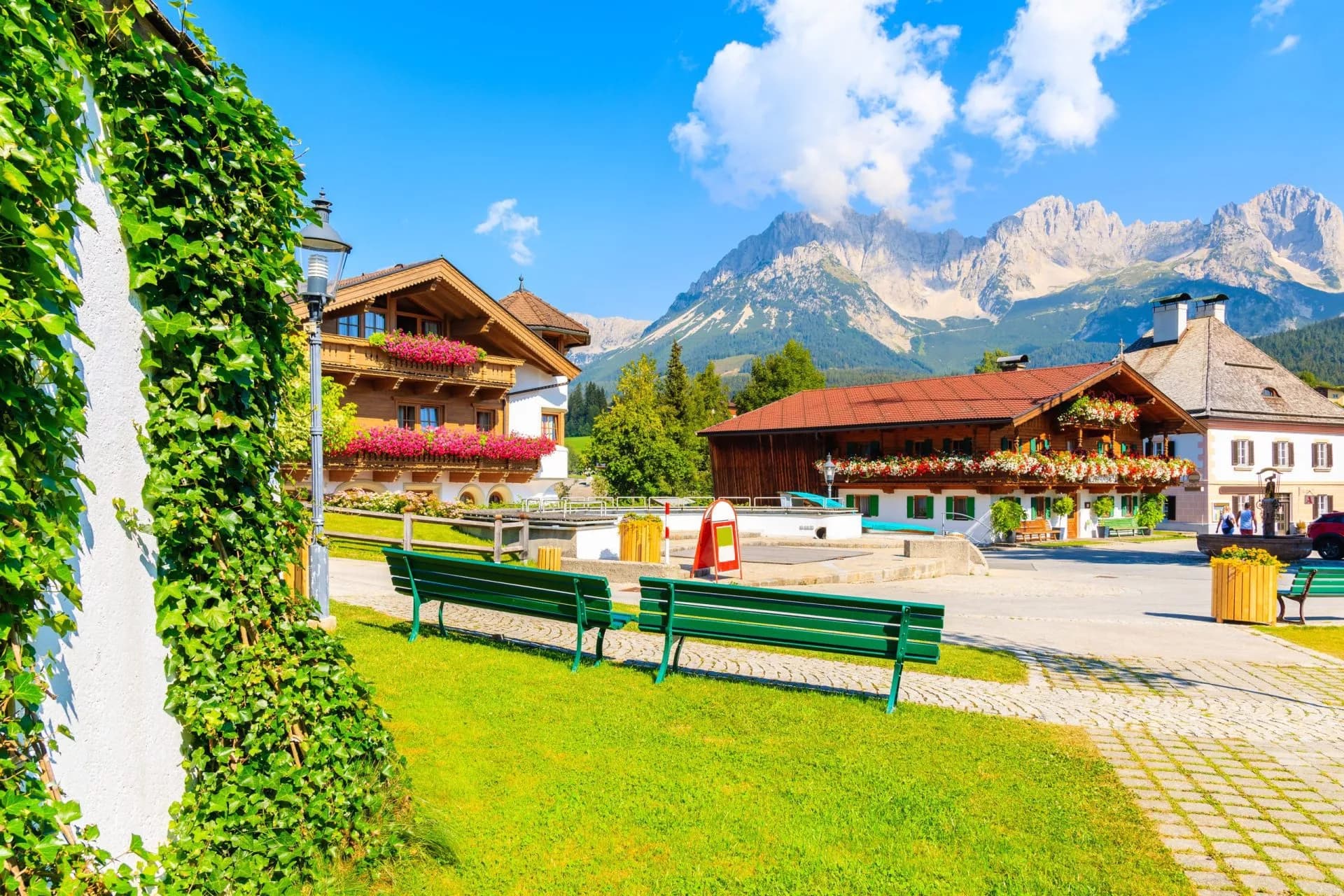 Traditional alpine houses on square in village of Going am Wilden Kaiser on beautiful sunny summer day with Alps mountains in background, Tirol, Austria
