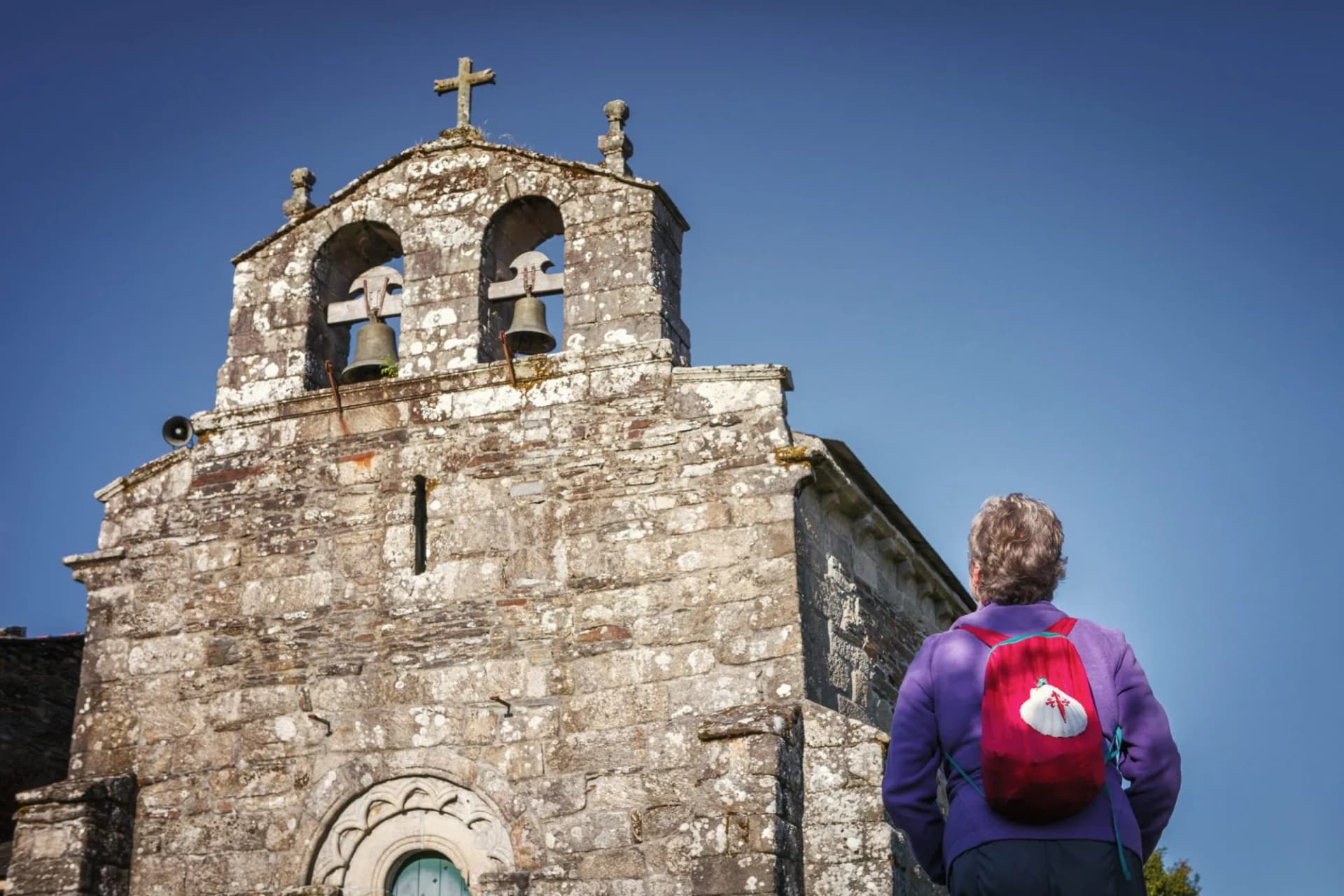 On the Way of St. James a pilgrim contemplates the beauty of the church of Santiago in Baamonde, Spain. Built in the 9th century until the 15th century.