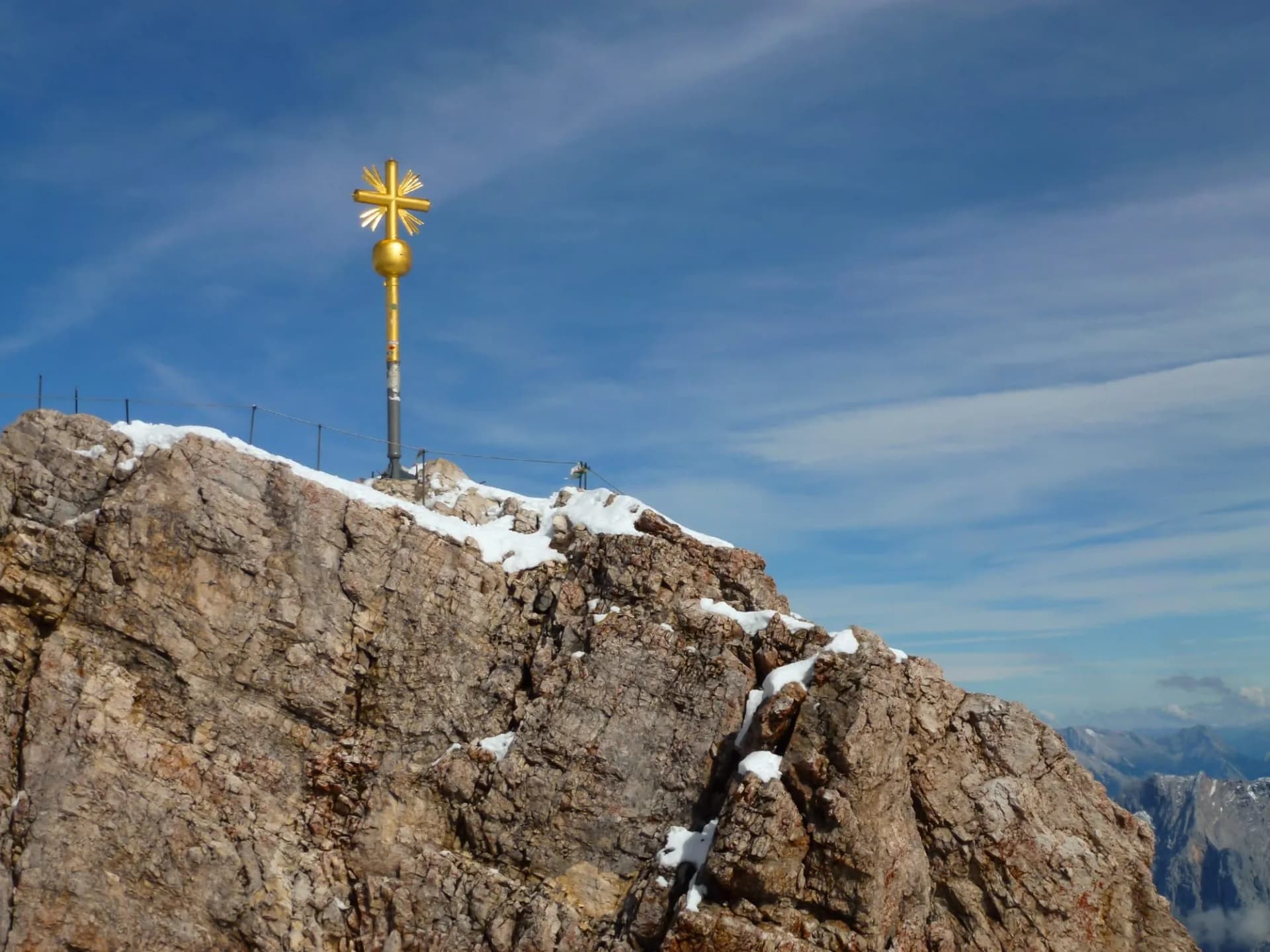A picturesque view of the iron yellow cross installed on the mountain against the background of the blue sky. Mountain peak in Bavaria, Germany