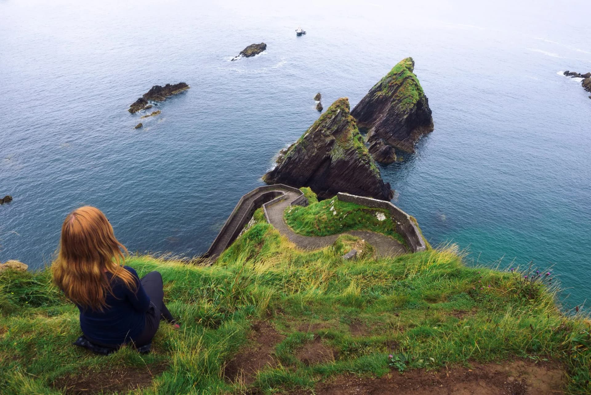 Girl sits on a cliff over the ocean in Ireland