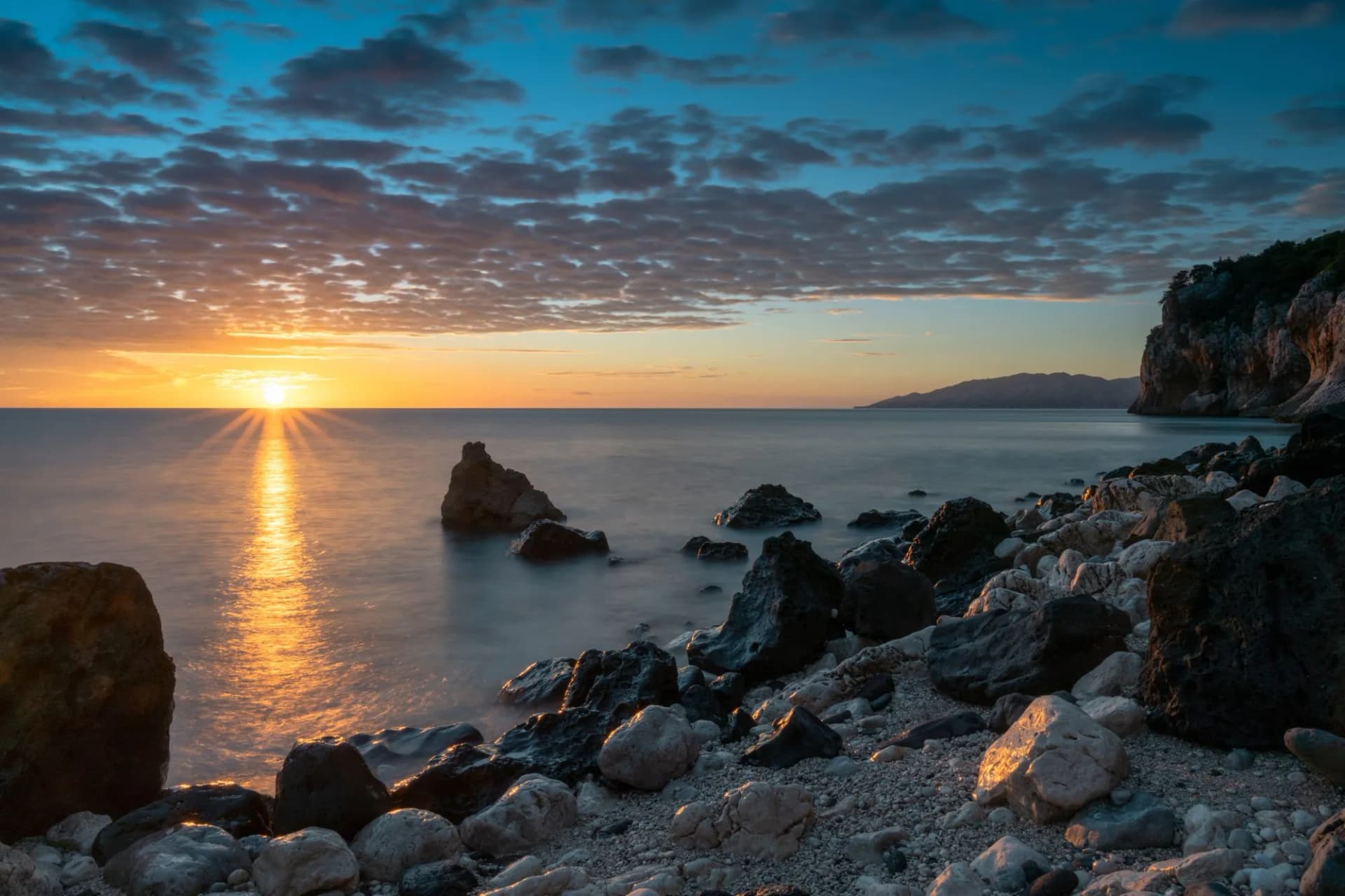 colorful sunrise at Cala Gonone with black and white rocks and boulders and a sunburst